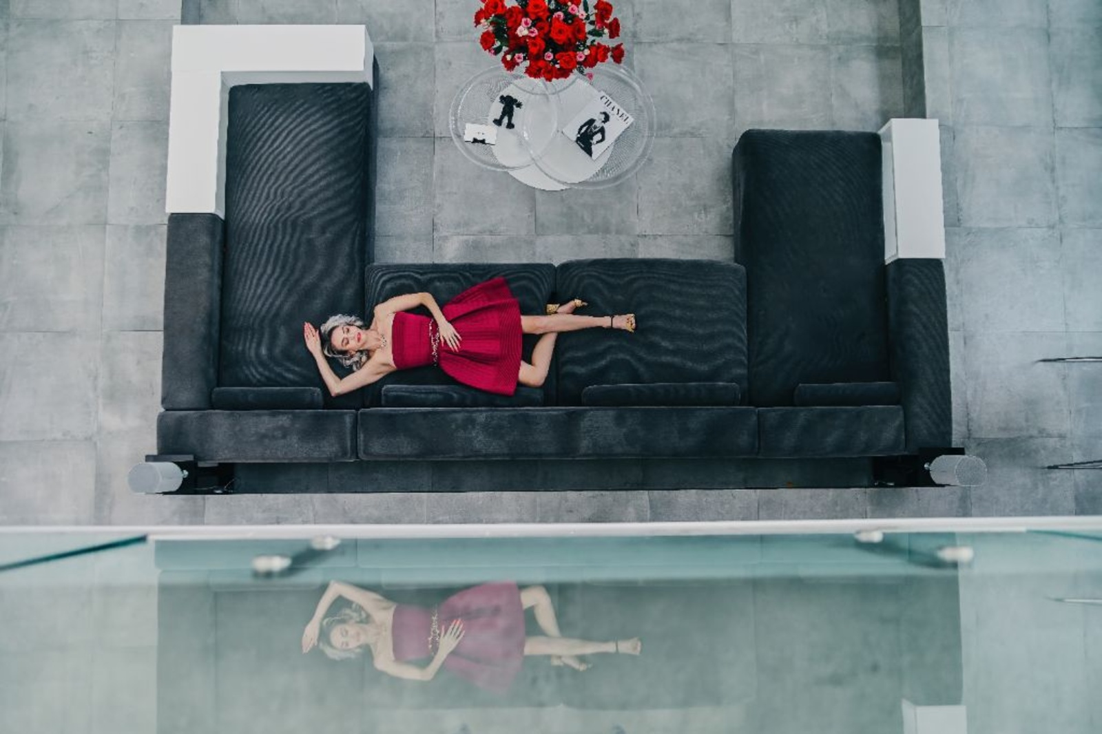 Lee Davies — overhead editorial · Chanel coffee-table books, red roses, charcoal sofa, mirrored pool
